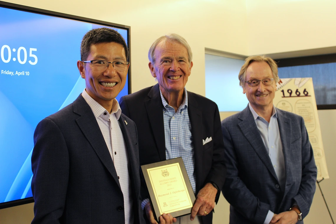 Three men with the center one receiving an award. 